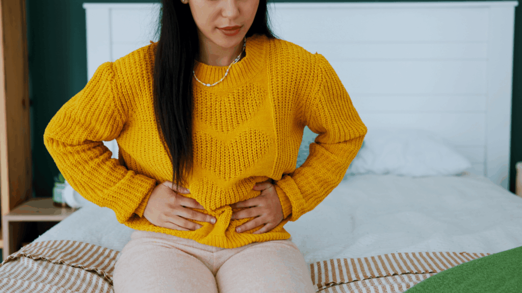 Woman in yellow shirt holding stomach, symbolizing pelvic pain and endometriosis symptoms
